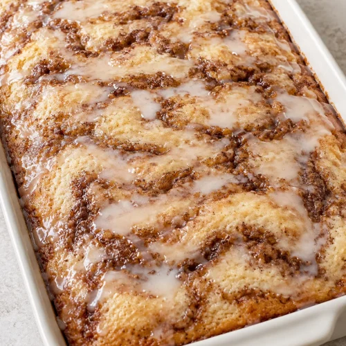Whole glazed Cinna-bun cake with brown cinnamon swirls in a baking dish