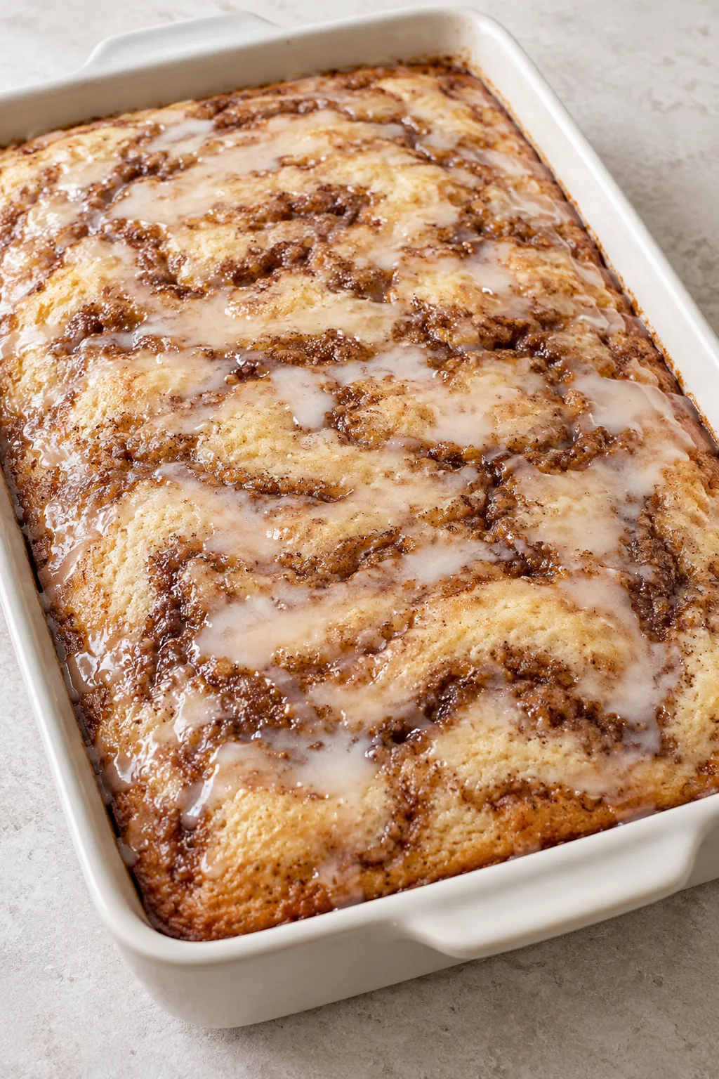 Whole glazed Cinna-bun cake with brown cinnamon swirls in a baking dish
