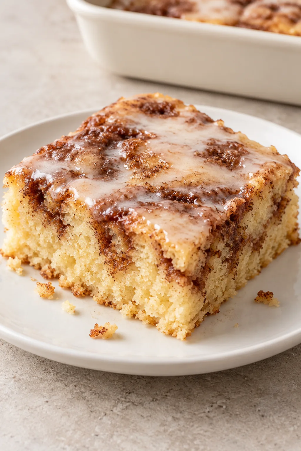 Square slice of Cinna-bun cake showing vanilla crumb, cinnamon pockets, and glaze