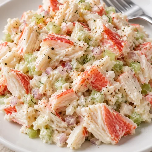 A portion of creamy crab seafood salad with imitation crab pieces and finely minced celery on a white plate