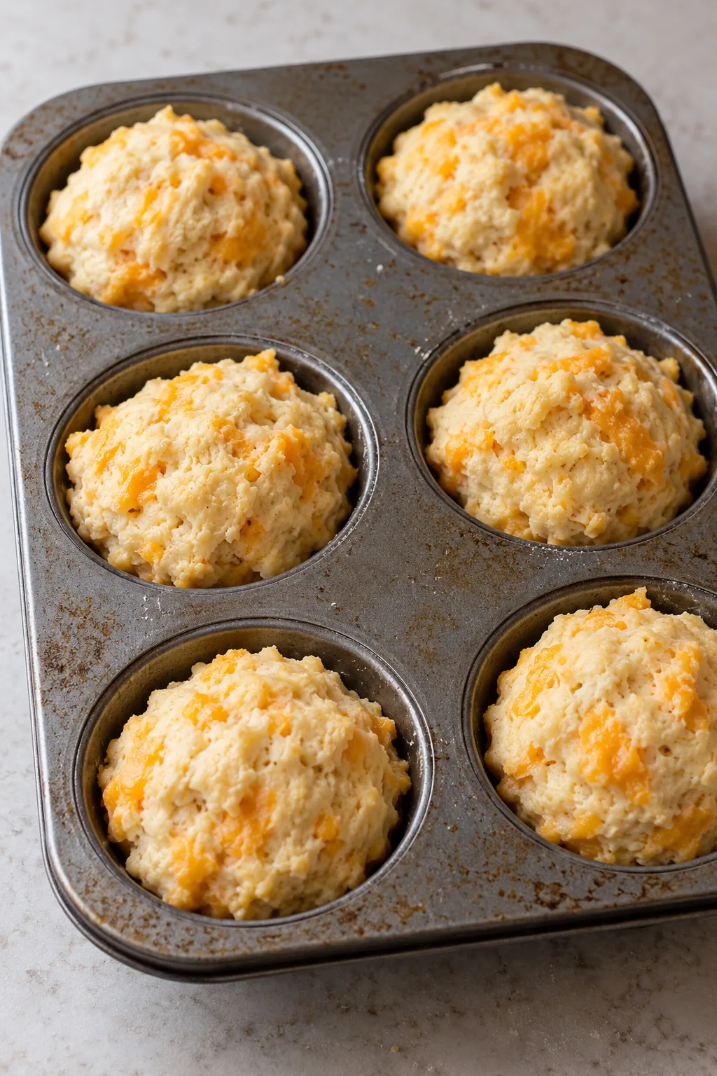 Unbaked crab stuffed cheddar biscuits sealed in a muffin tin