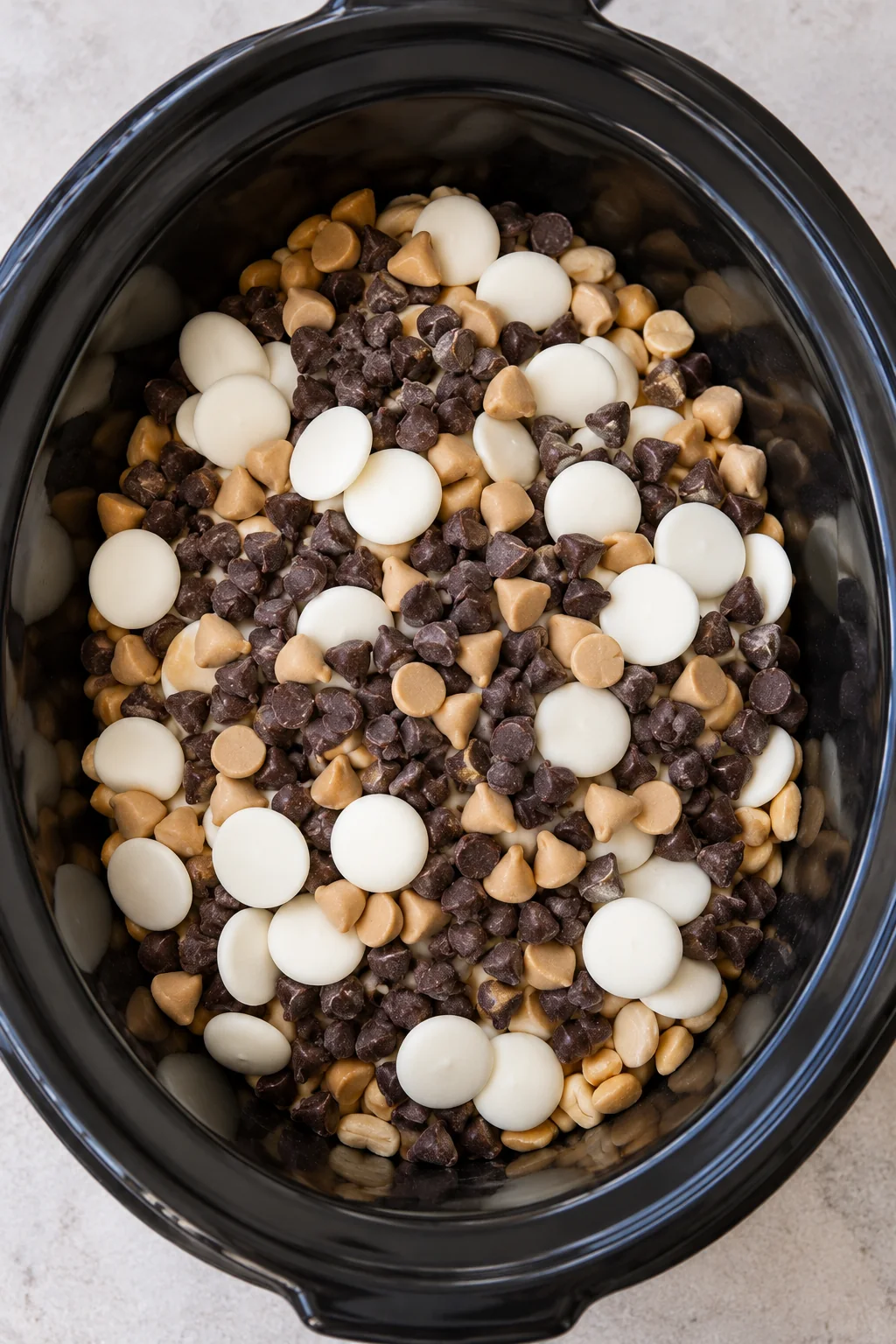 Unmelted chocolate chips, peanut butter chips, and white wafers layered over peanuts