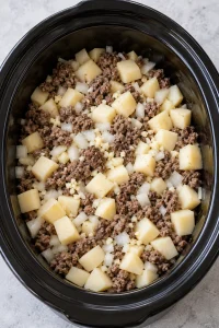 Browned beef, diced potatoes, onion and garlic in the slow cooker before adding broth.
