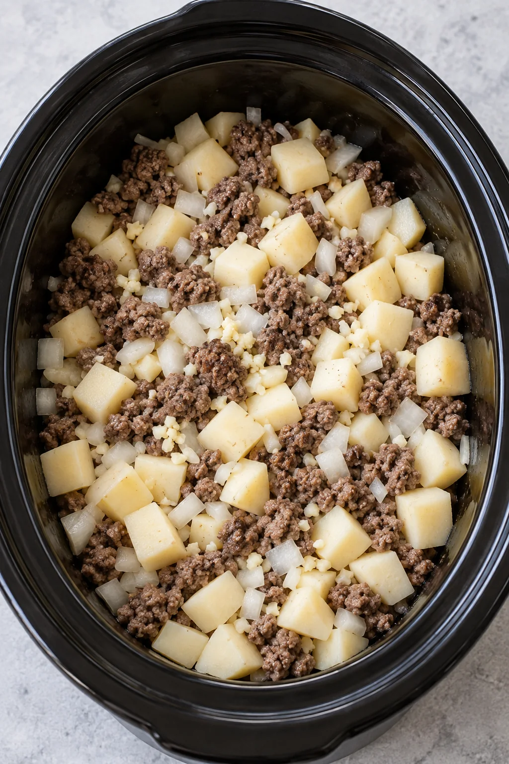 Browned beef, diced potatoes, onion and garlic in the slow cooker before adding broth.