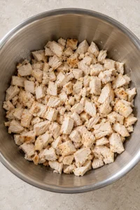 Small bite-size pieces of cooked chicken in a stainless mixing bowl