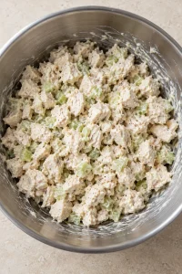 Diced chicken and celery evenly coated with mayonnaise in a stainless bowl
