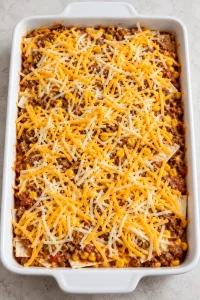 Assembled burrito casserole covered with shredded taco-blend cheese before baking
