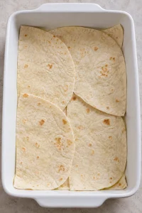 Flour tortilla halves overlapping across the bottom of a greased baking dish