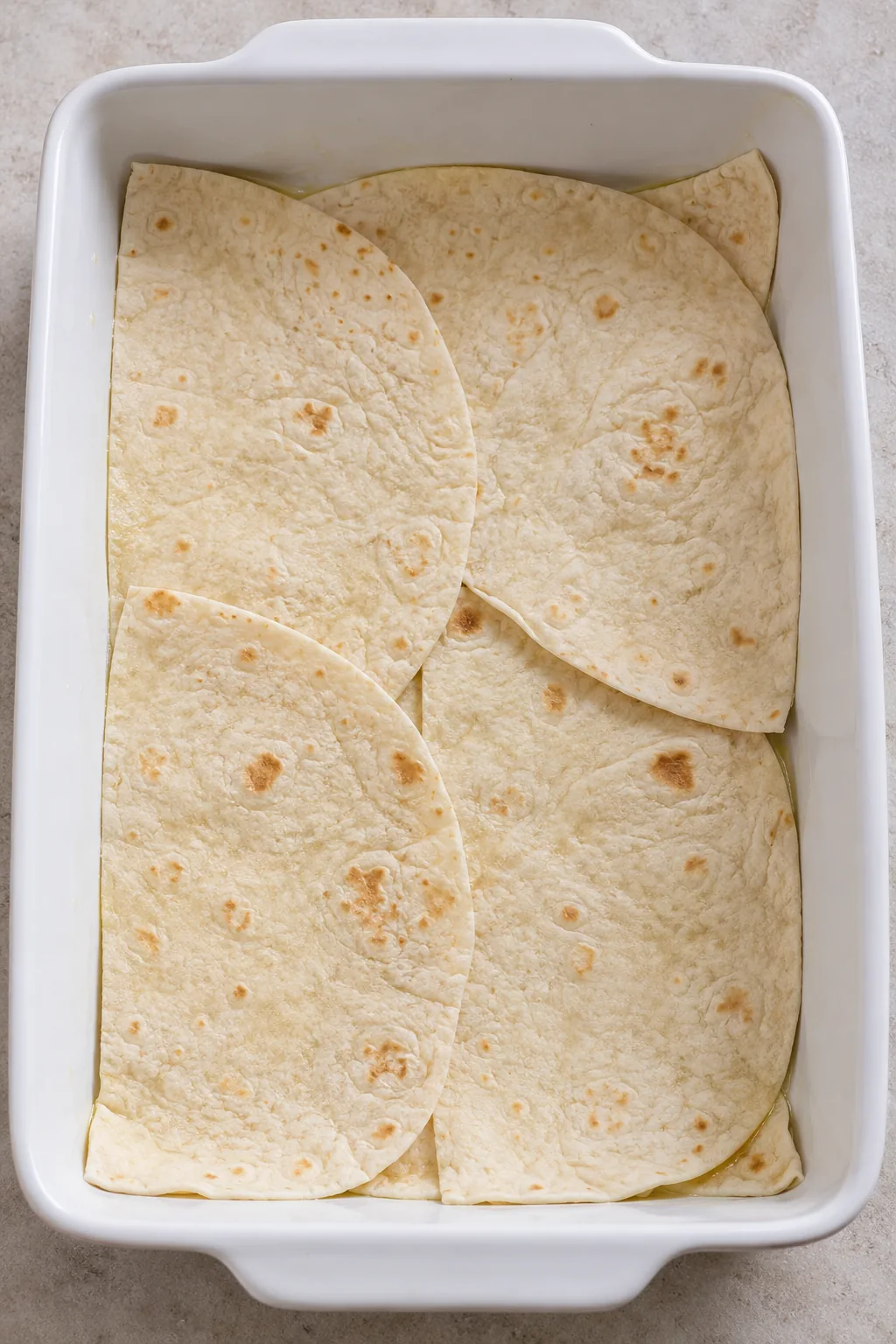 Flour tortilla halves overlapping across the bottom of a greased baking dish
