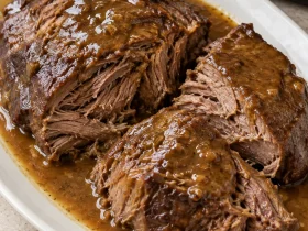 Tender chuck roast in large pieces with brown gravy on an ivory platter