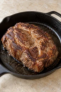 A thick chuck roast with a browned crust in a cast-iron skillet