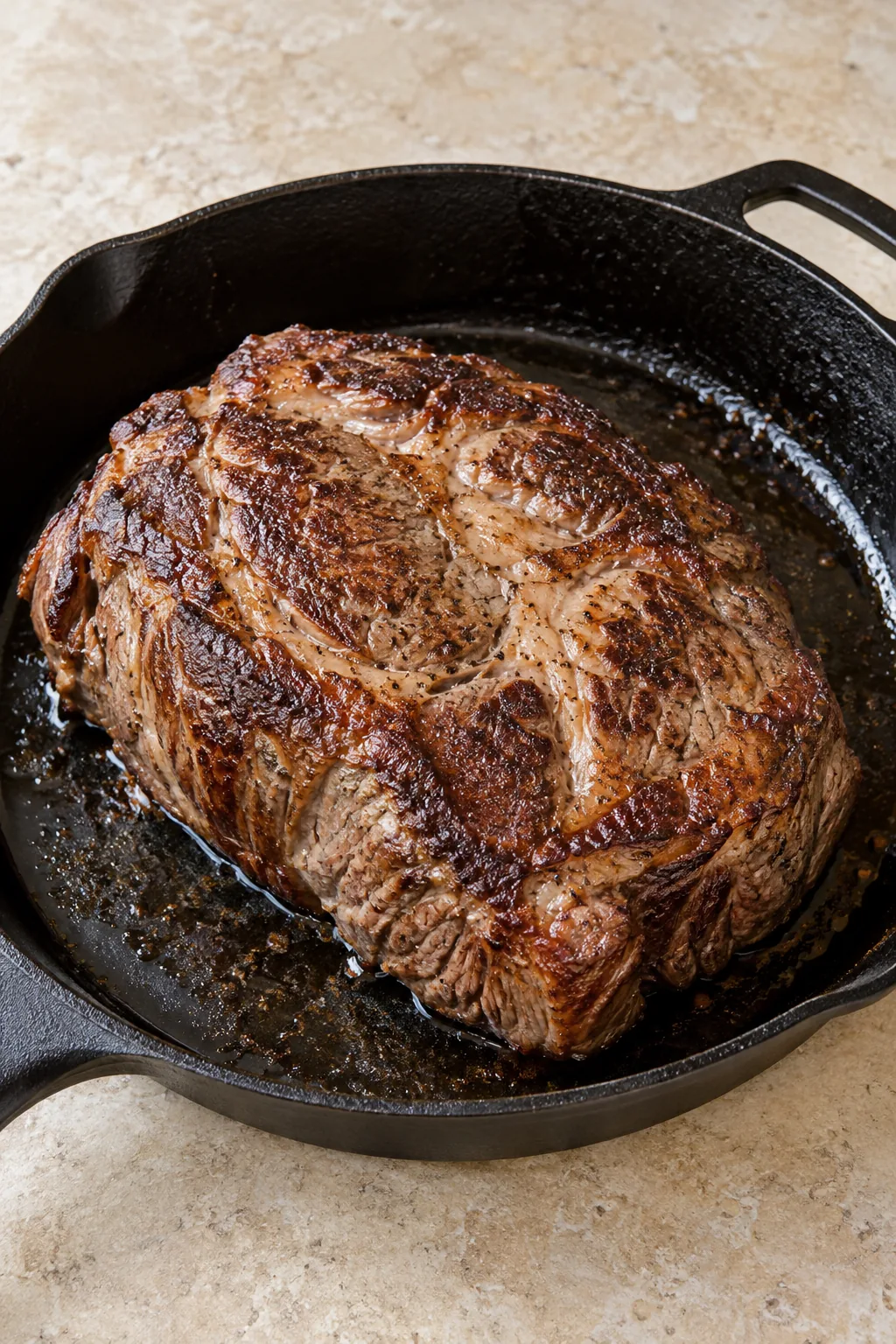 A thick chuck roast with a browned crust in a cast-iron skillet
