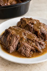 Close view of moist pot roast pieces coated with brown gravy on a white plate