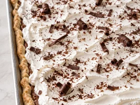 Whole French silk slab pie topped with whipped cream and chocolate shavings in a shallow sheet pan.