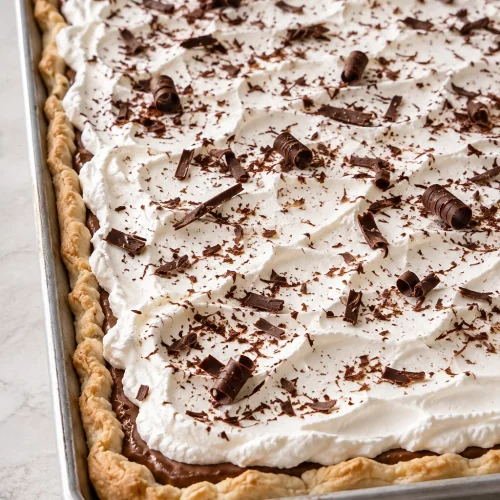 Whole French silk slab pie topped with whipped cream and chocolate shavings in a shallow sheet pan.