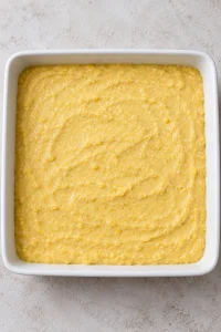 Unbaked buttermilk cornbread batter spread in an eight-inch square pan