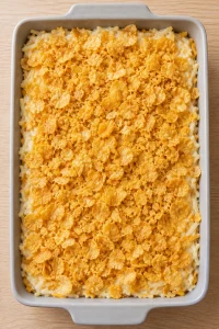 Unbaked hashbrown casserole covered with buttered cornflakes before baking