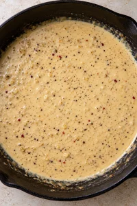 Smooth creamy garlic Parmesan sauce with fine pepper flecks in the skillet.