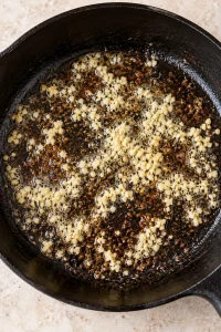 Minced garlic cooking in butter with browned steak drippings in the skillet.