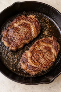 Two ribeye steaks with browned crusts in a cast-iron skillet.