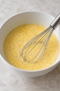 Eggs, milk and seasonings whisked into a pale yellow mixture in a white bowl
