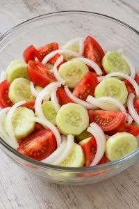 Sliced cucumbers, tomato wedges and onion rings in the mixing bowl before dressing.