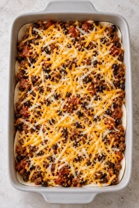 First tortilla layer covered with beef and bean filling and shredded cheese