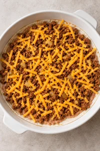 Refried beans, seasoned ground beef and shredded cheddar covering the first tortilla layer