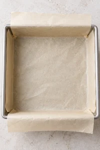 An empty square metal pan lined with creased parchment paper before making fudge