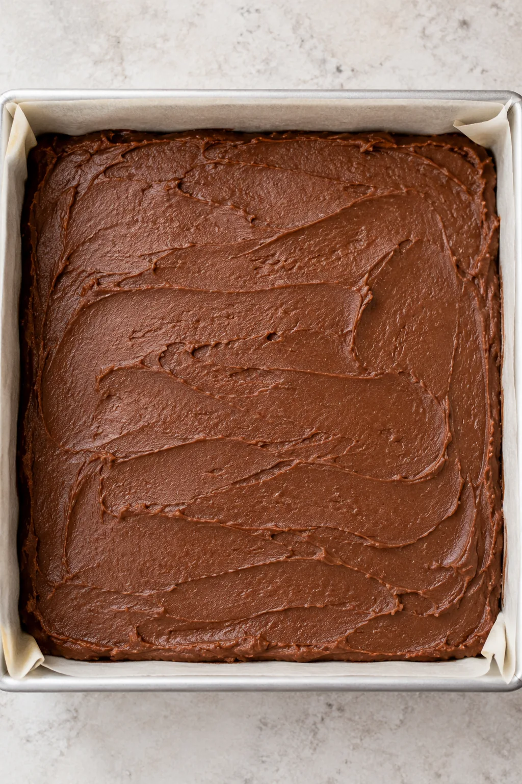 Uncut plain chocolate fudge spread into a parchment-lined square pan with soft spatula ridges