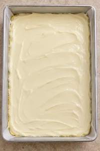 Unbaked cream cheese topping spread over the yellow cake-mix crust