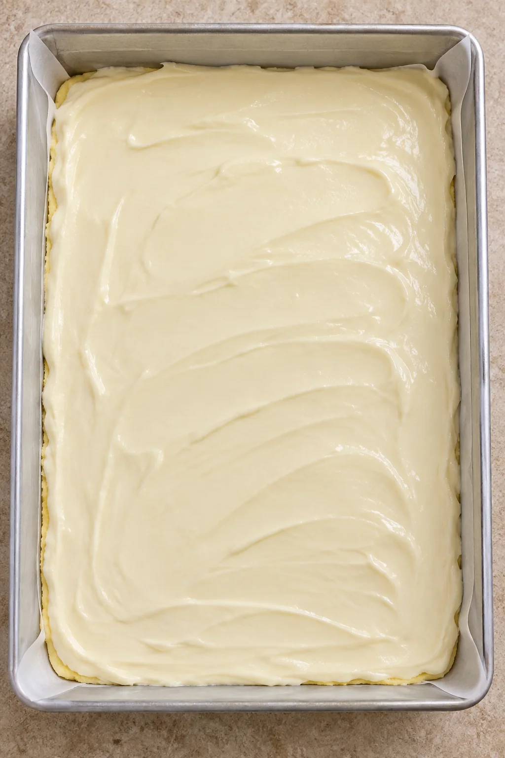 Unbaked cream cheese topping spread over the yellow cake-mix crust