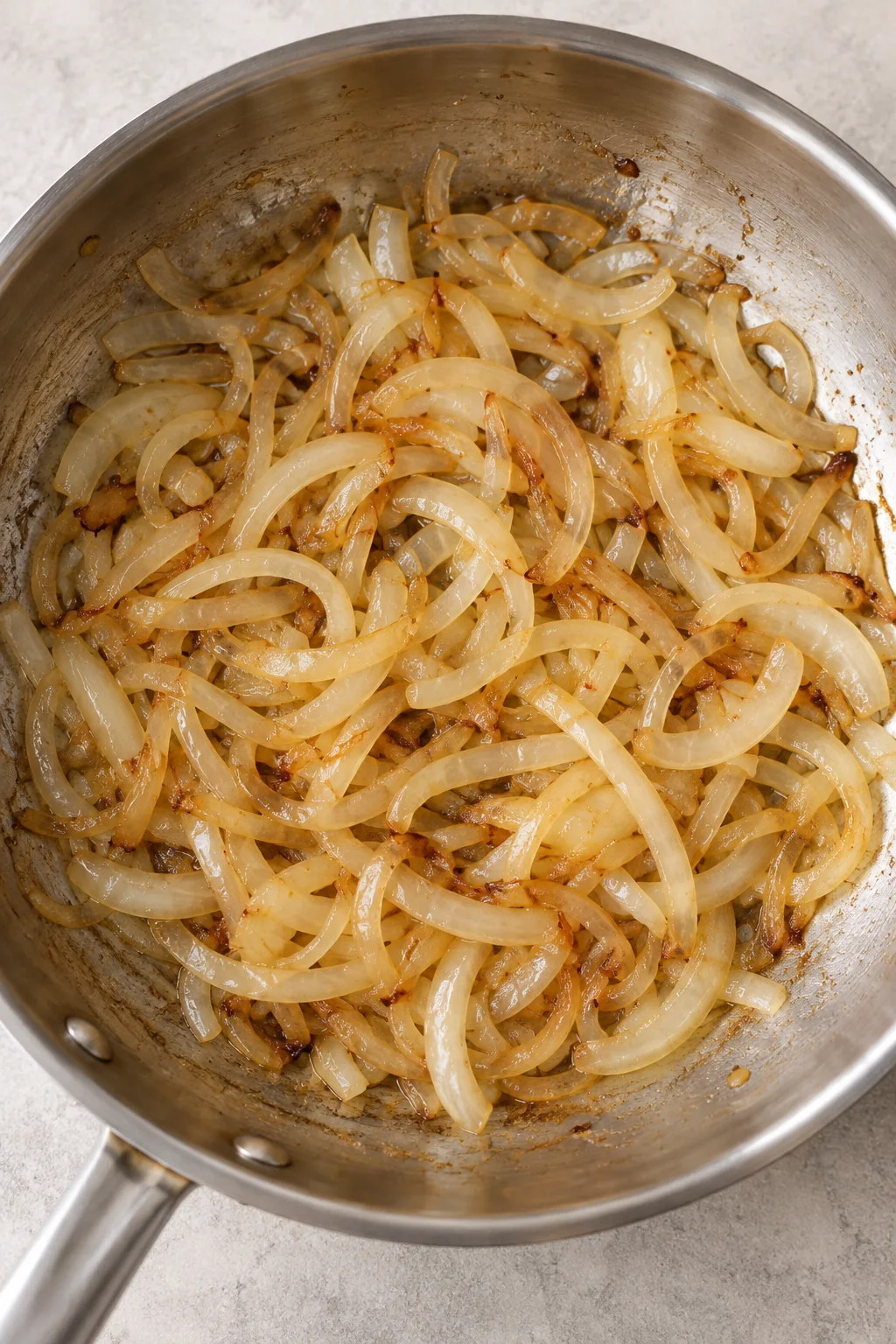 Sliced onions softening and beginning to turn golden in a stainless steel skillet