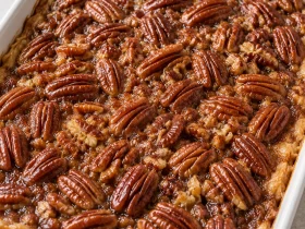 Whole pecan pie cobbler topped with toasted pecan halves in a white baking dish