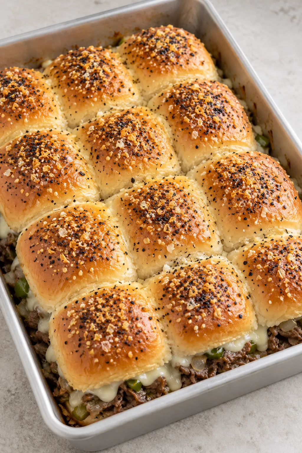 A whole tray of twelve Philly cheesesteak sliders with an everything-seasoned butter topping