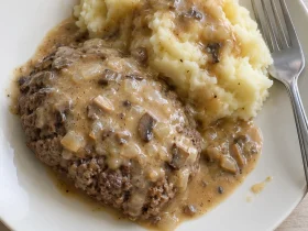 Slow cooker hamburger steak with mushroom-onion gravy and mashed potatoes on a plain plate
