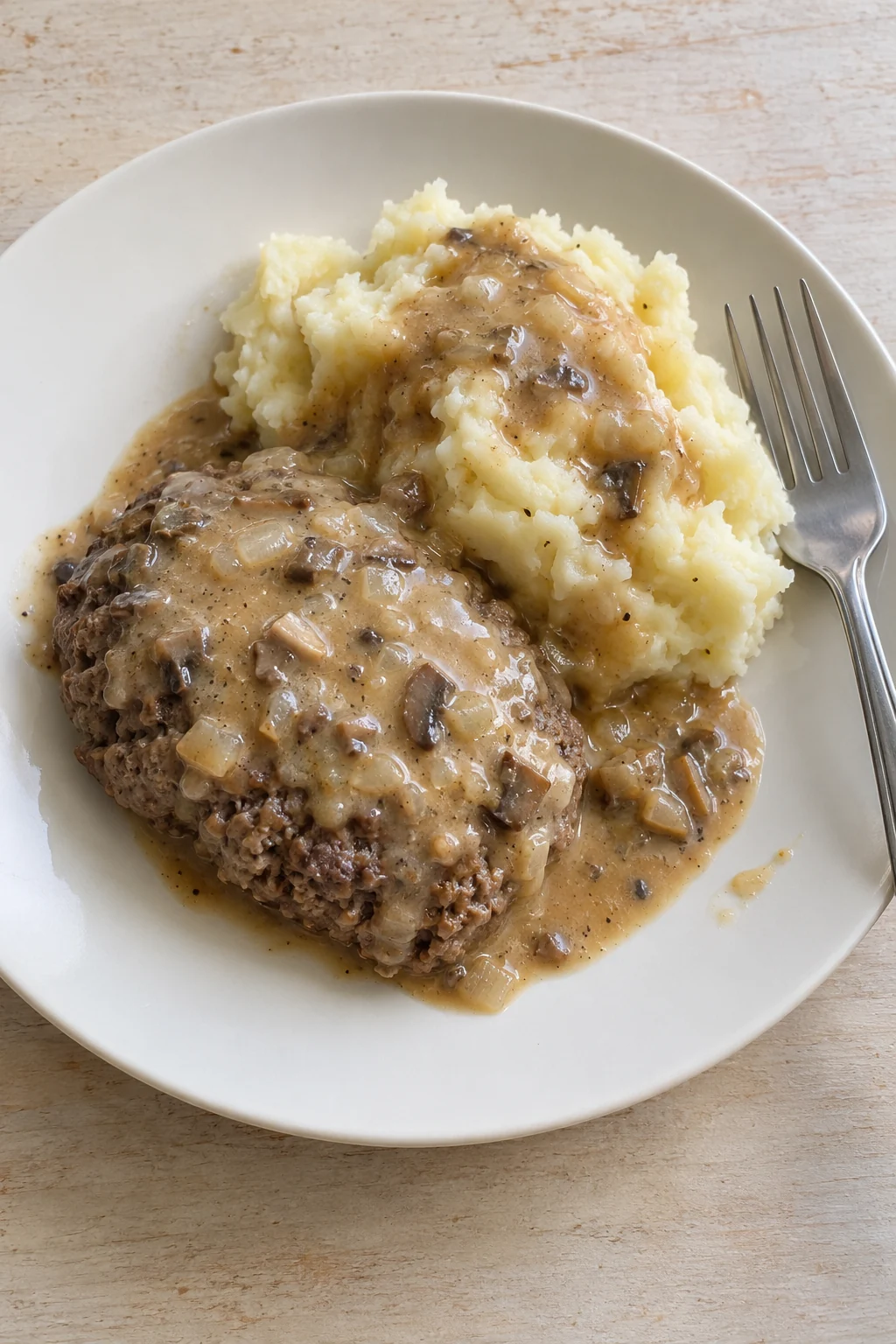 Slow cooker hamburger steak with mushroom-onion gravy and mashed potatoes on a plain plate