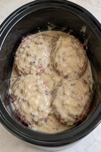 Four raw patties covered with mushroom-onion gravy in an oval slow cooker