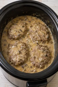 Four cooked hamburger steaks in mushroom-onion gravy in a black slow cooker