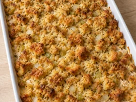 Whole rotisserie chicken and stuffing casserole with a golden bread topping in a white baking dish