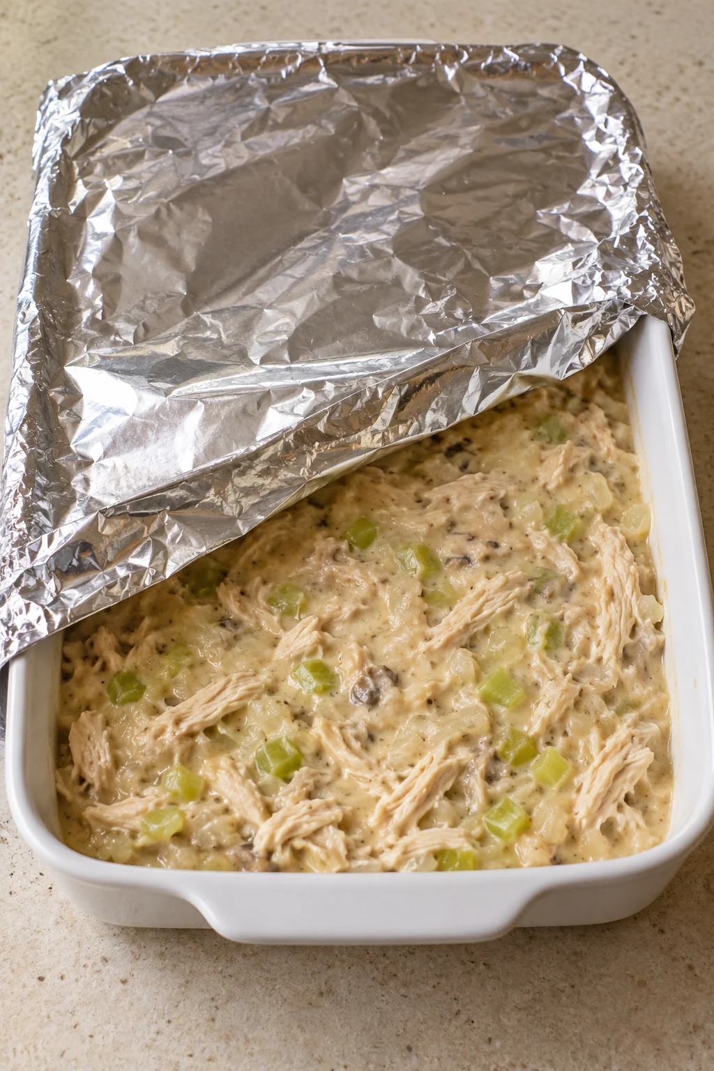 Creamy chicken casserole base partly covered with foil before adding the stuffing