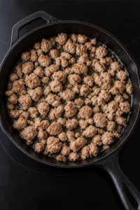 Browned breakfast sausage crumbles with rendered fat in a cast-iron skillet