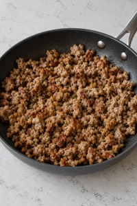 Cooked pork sausage broken into small browned crumbles in a skillet