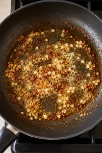 Minced garlic softening in butter with browned paprika bits in the skillet