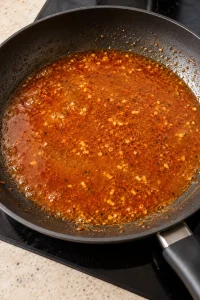 Thin orange-red lemon-garlic paprika sauce simmering in the skillet after the chicken is removed
