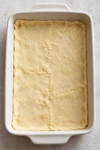 Raw crescent dough pressed into the bottom of a rectangular baking dish with the seams sealed.
