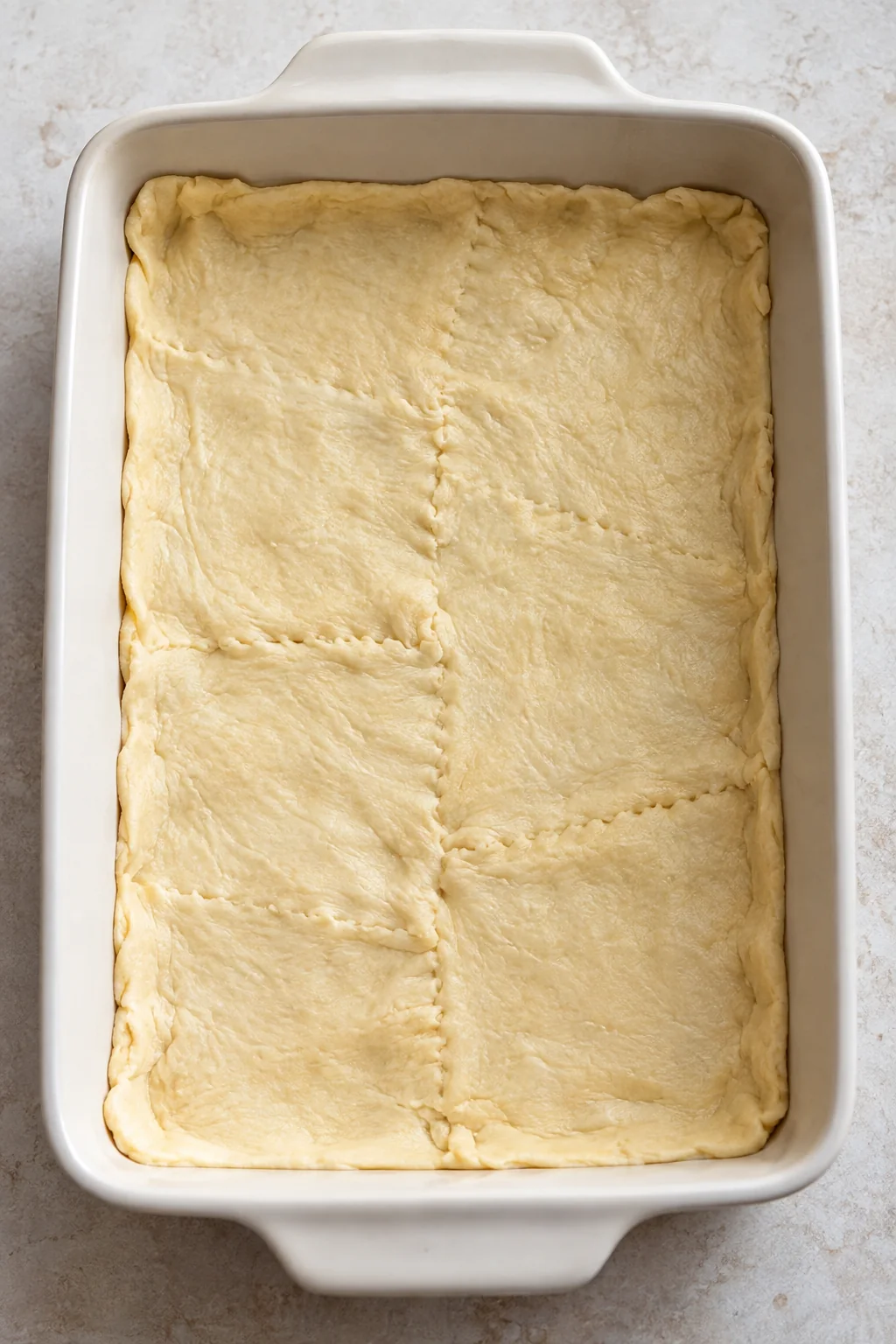 Raw crescent dough pressed into the bottom of a rectangular baking dish with the seams sealed.