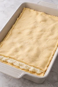 Second raw crescent dough sheet covering the cheesecake filling.