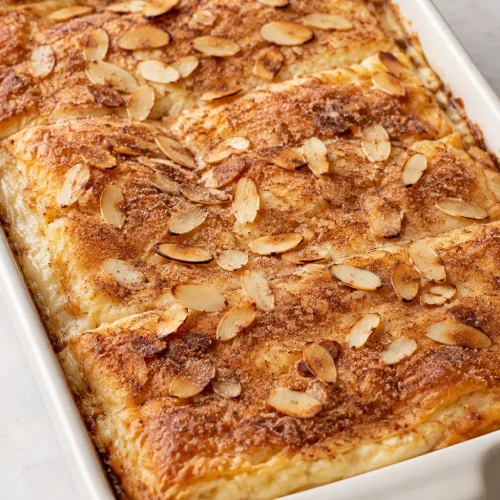 Whole sopapilla cheesecake with cinnamon sugar and toasted sliced almonds in a rectangular baking dish.
