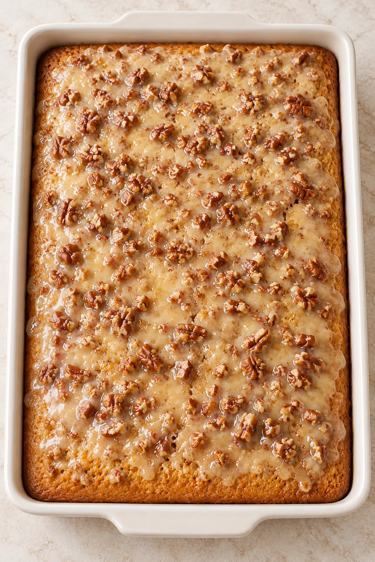 Overhead view of an uncut pecan sheet cake topped with chopped pecans and creamy glaze